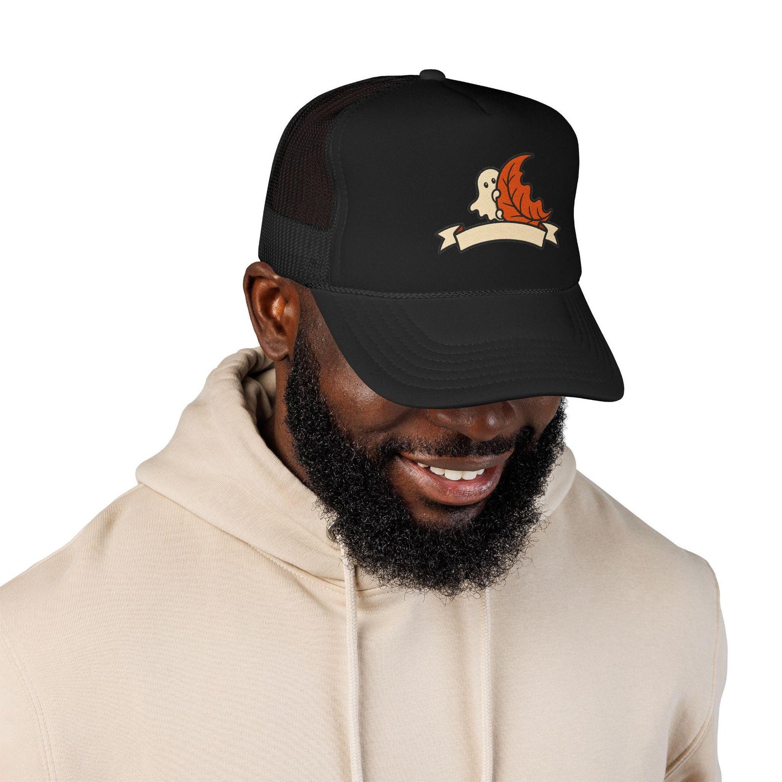 Smiling man in a beige hoodie wearing the black ghost and autumn leaf foam trucker hat